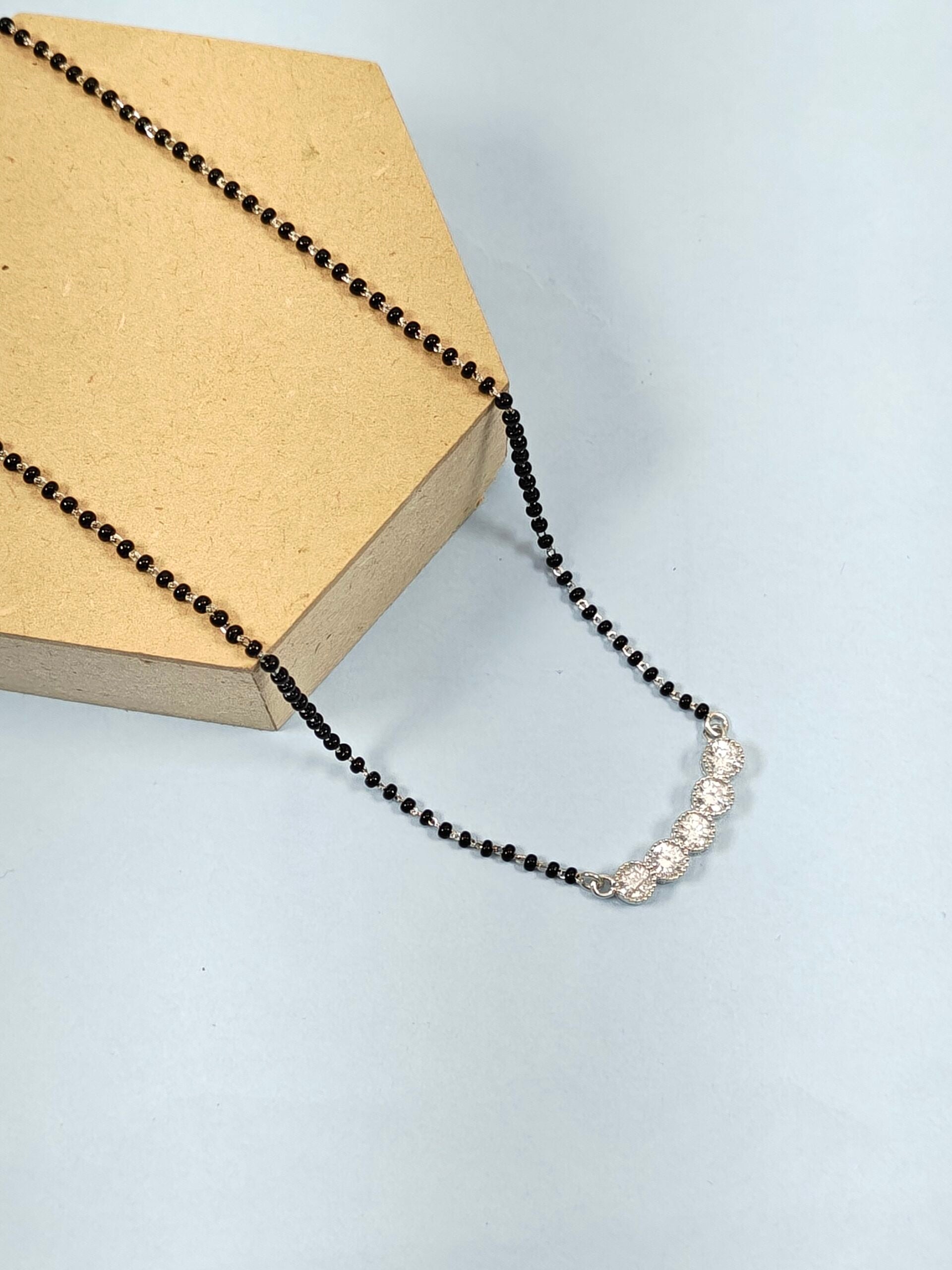 Necklace with black beads and silver clasp on a light blue background